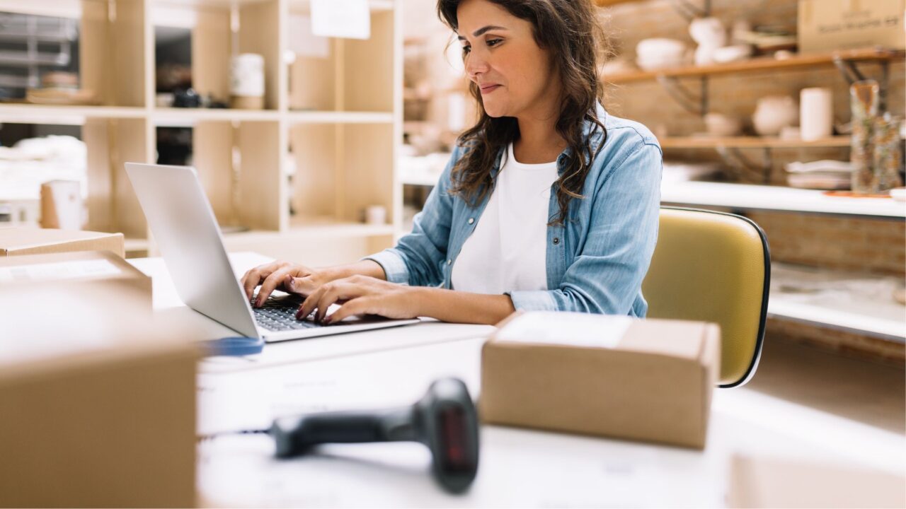 a woman working on a laptop with boxes all around her. 